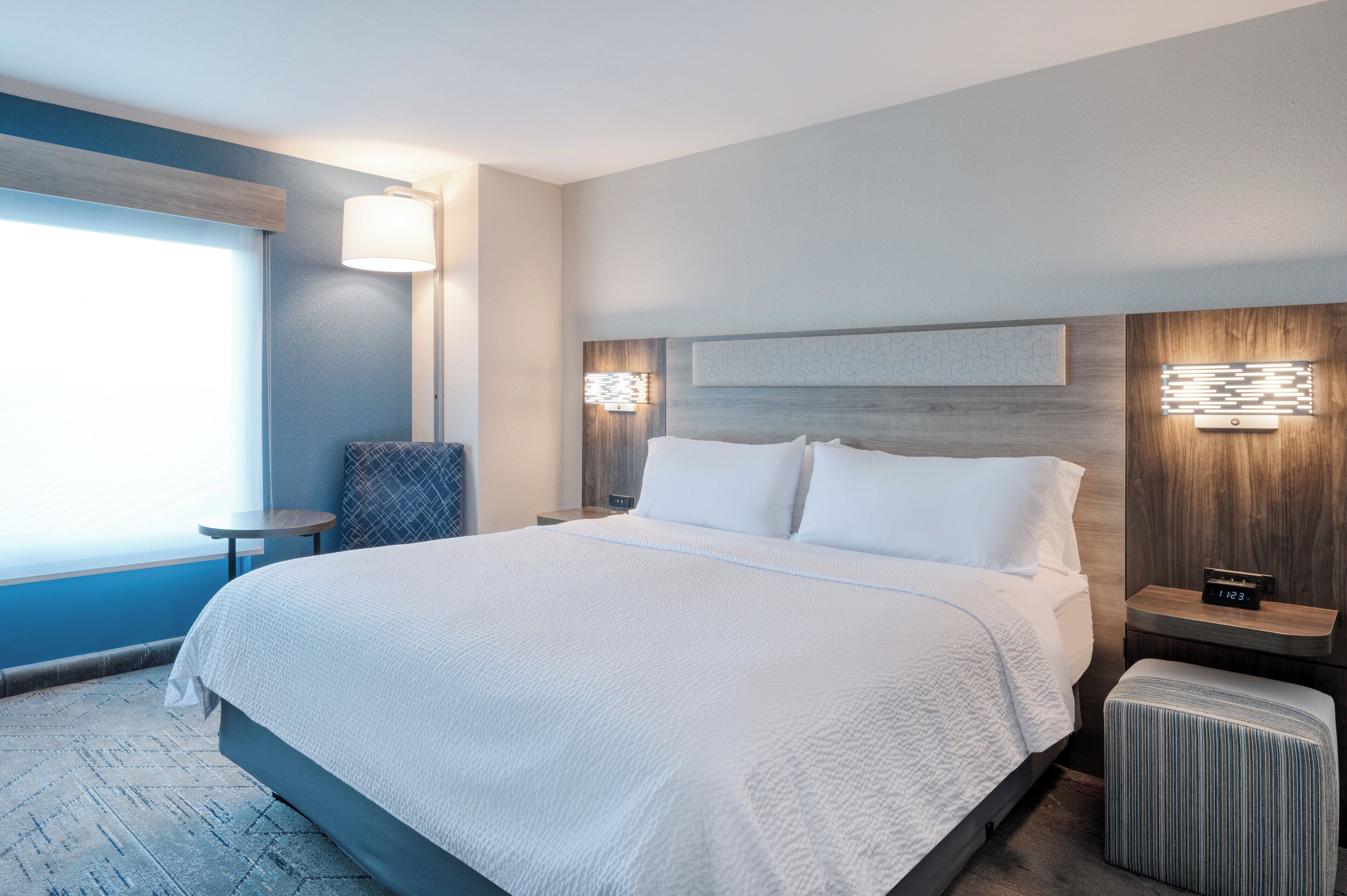 A hotel room with a large bed, bedside tables, a nightstand, a chair, and a view of the ocean.