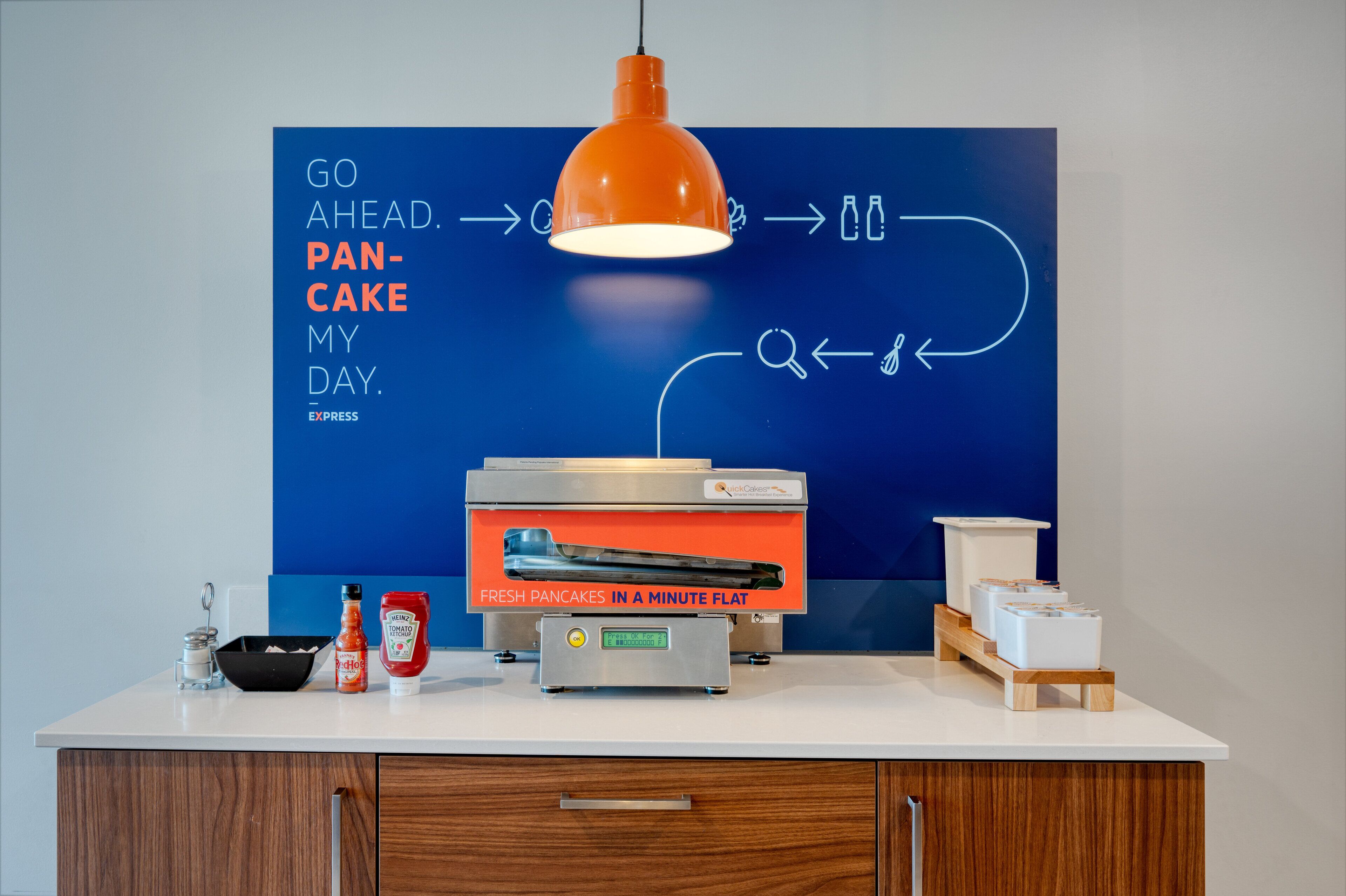 A kitchen counter with a flatbread toaster, a bottle of ketchup, and a bottle of tomato ketchup.