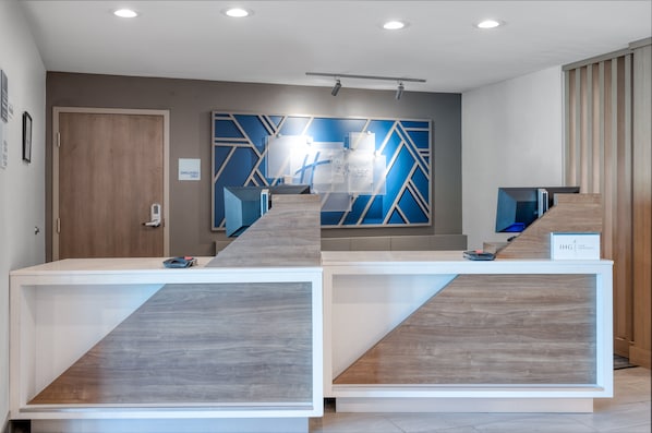 Uma área de recepção com design moderno, incluindo um balcão de atendimento, uma placa na parede e uma porta com a inscrição 'SOMENTE FUNCIONÁRIOS'.