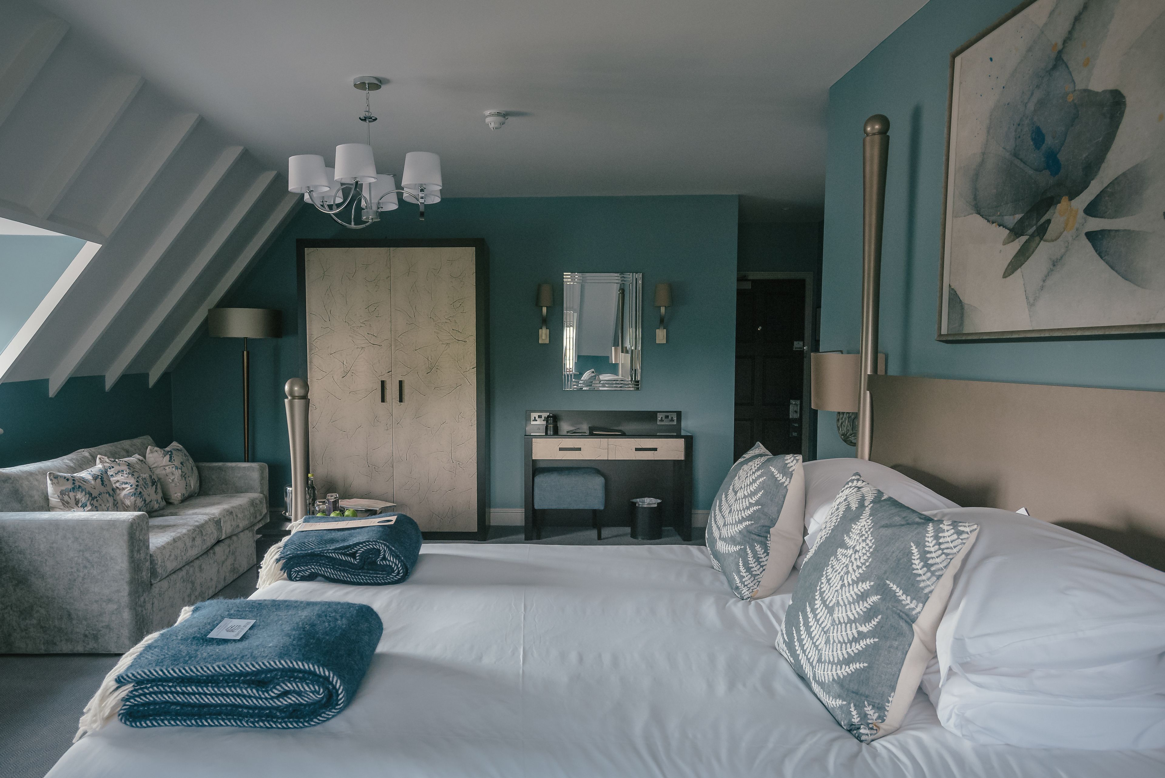 A modern hotel room with a large bed, a desk, a wardrobe, and a chandelier.
