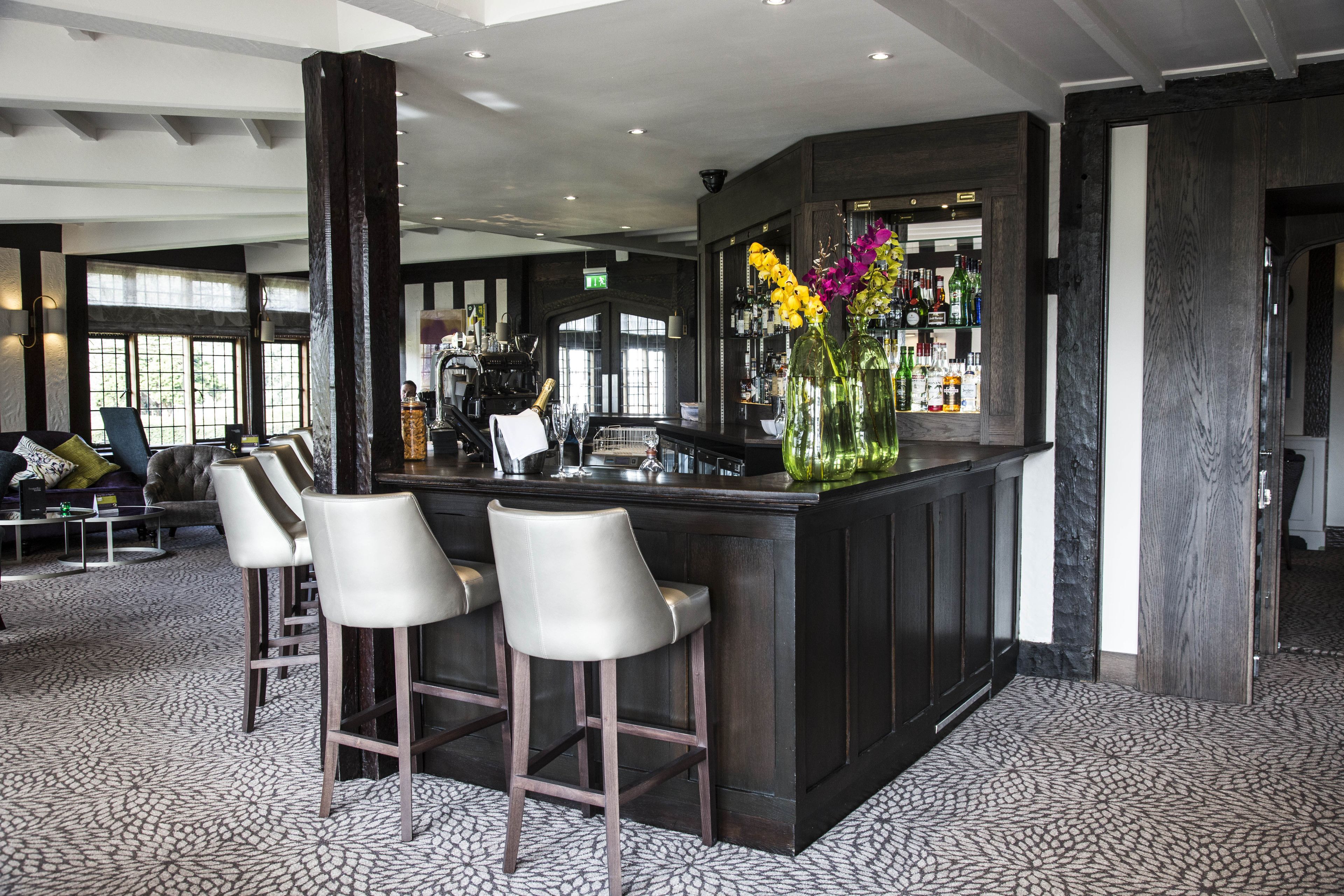 Una zona de bar con un mostrador de madera oscura, tres taburetes blancos y un florero decorativo con flores.