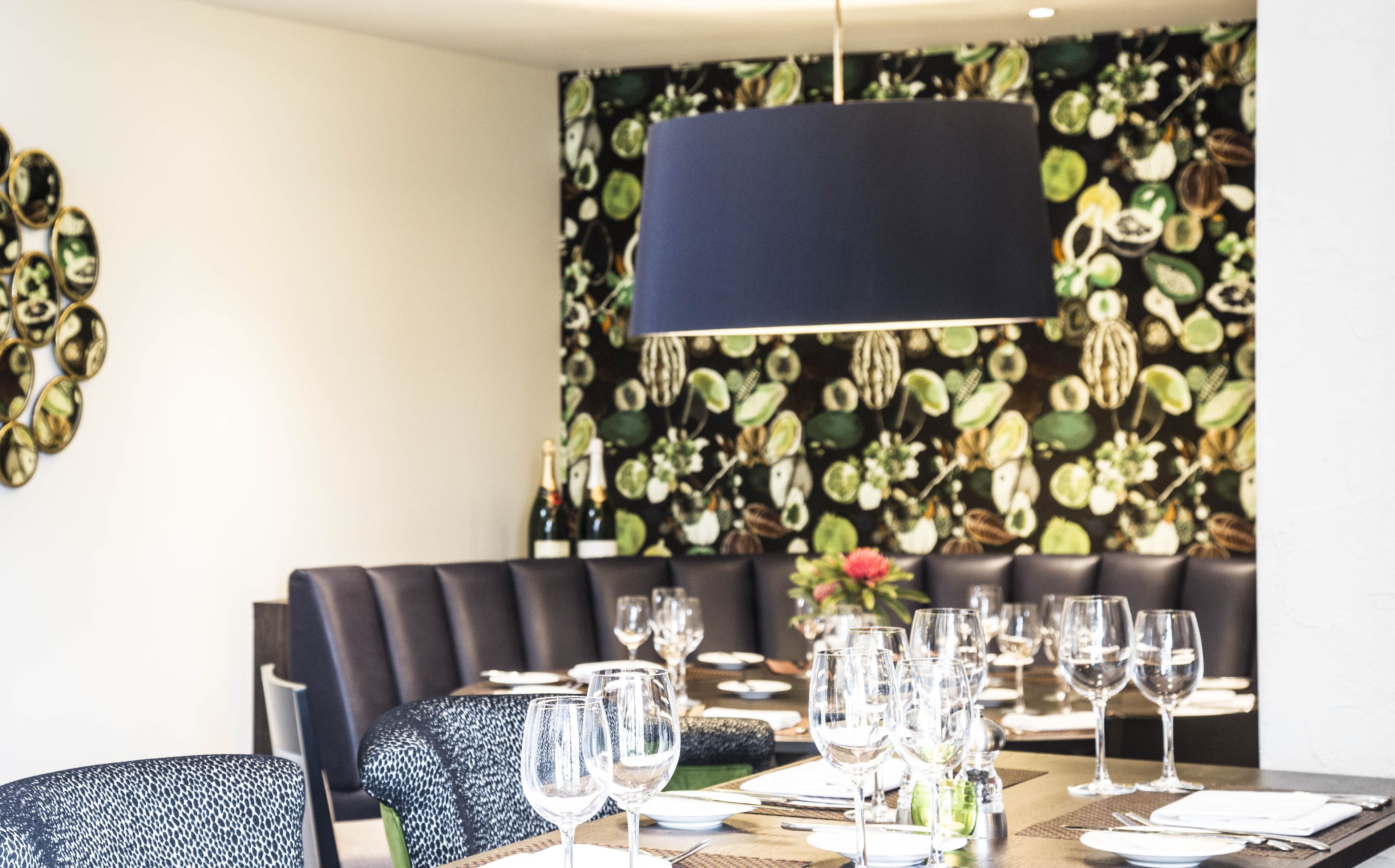 Zona pranzo con tavolo apparecchiato, lampadario blu scuro e parete decorata con motivi floreali.