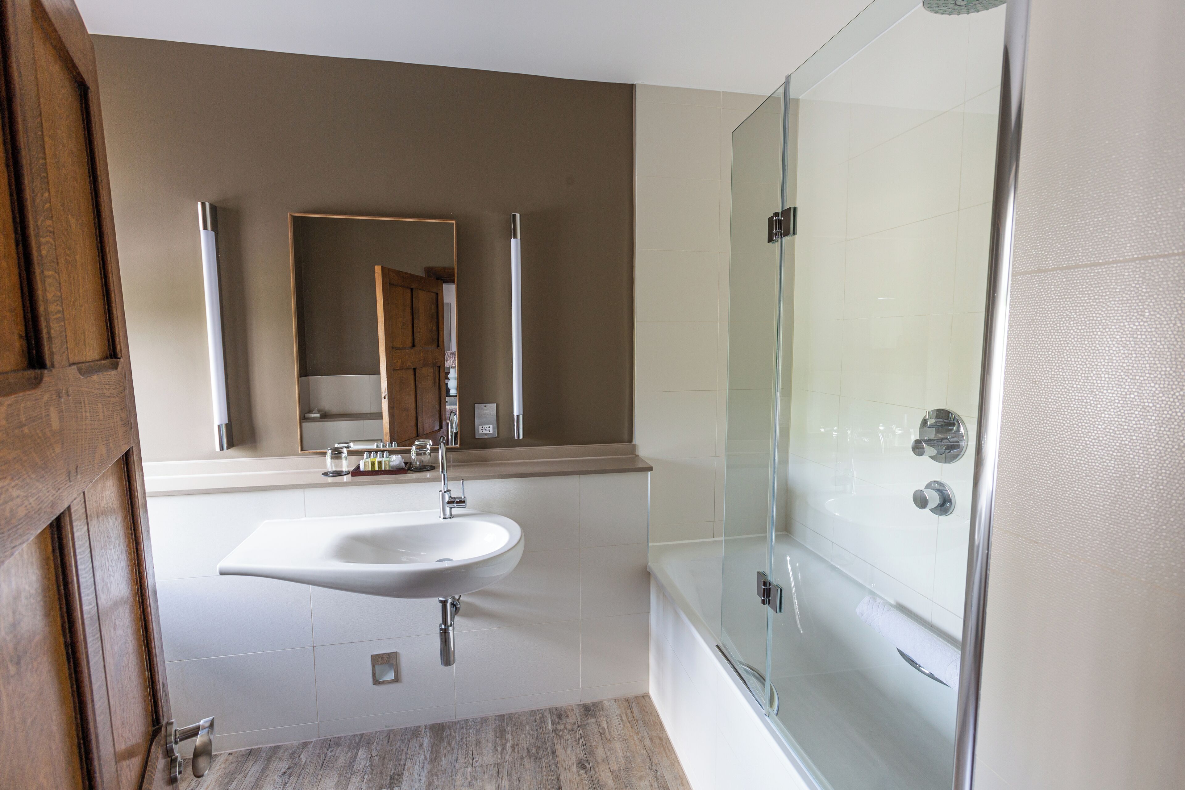 Un baño moderno con ducha de vidrio, un lavamanos blanco y una puerta de madera.
