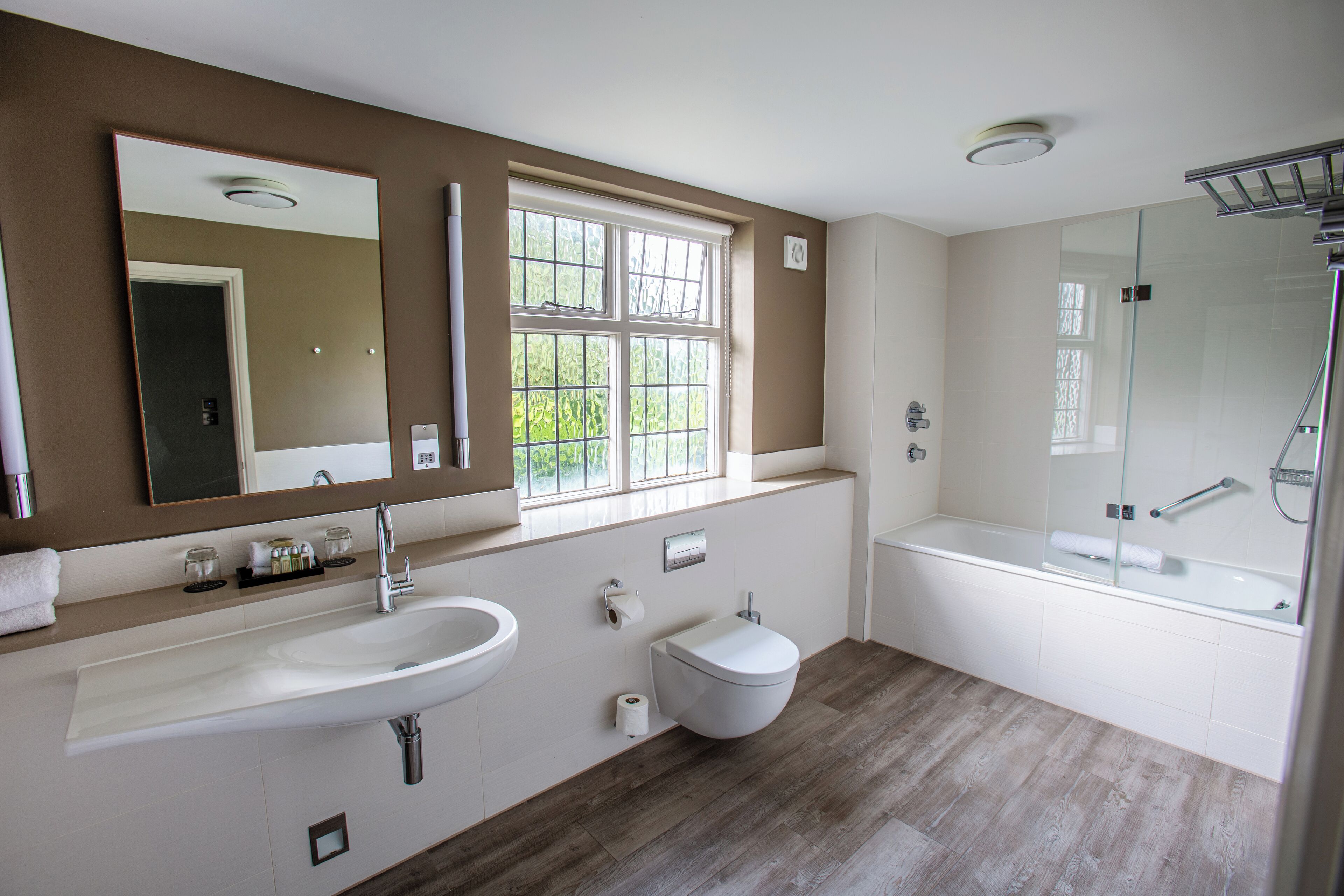 A modern bathroom with a large mirror, a sink, a toilet, and a glass-enclosed shower.
