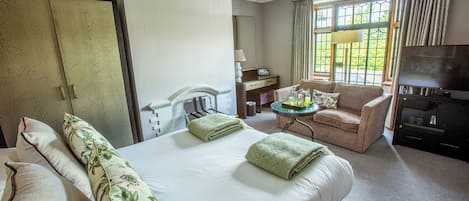 Habitación de hotel con una cama grande, una zona de estar con una silla y una mesita, televisión y ventana con cortinas.