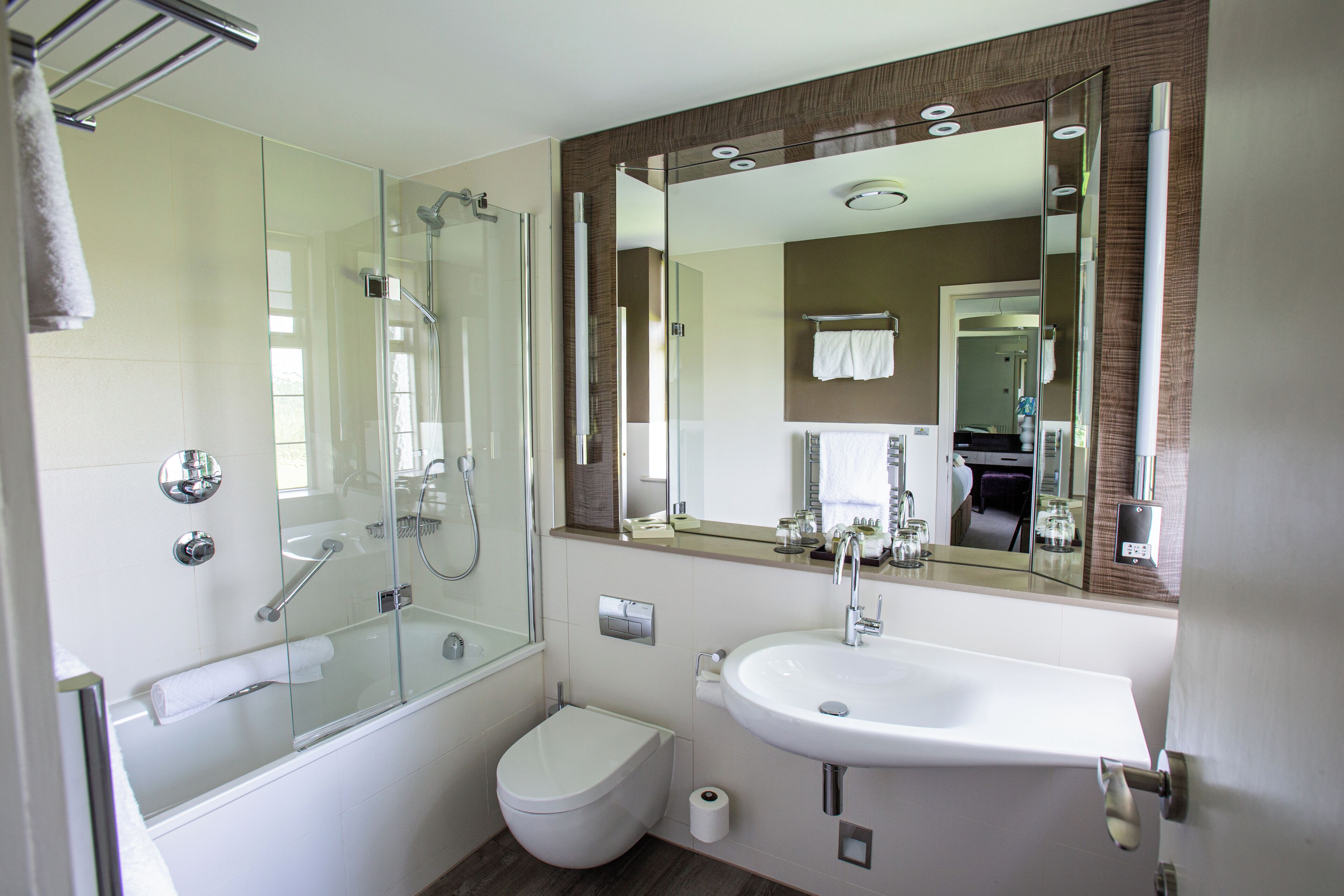 Un baño moderno con ducha envuelta en vidrio, inodoro blanco y lavamanos con un espejo grande arriba.