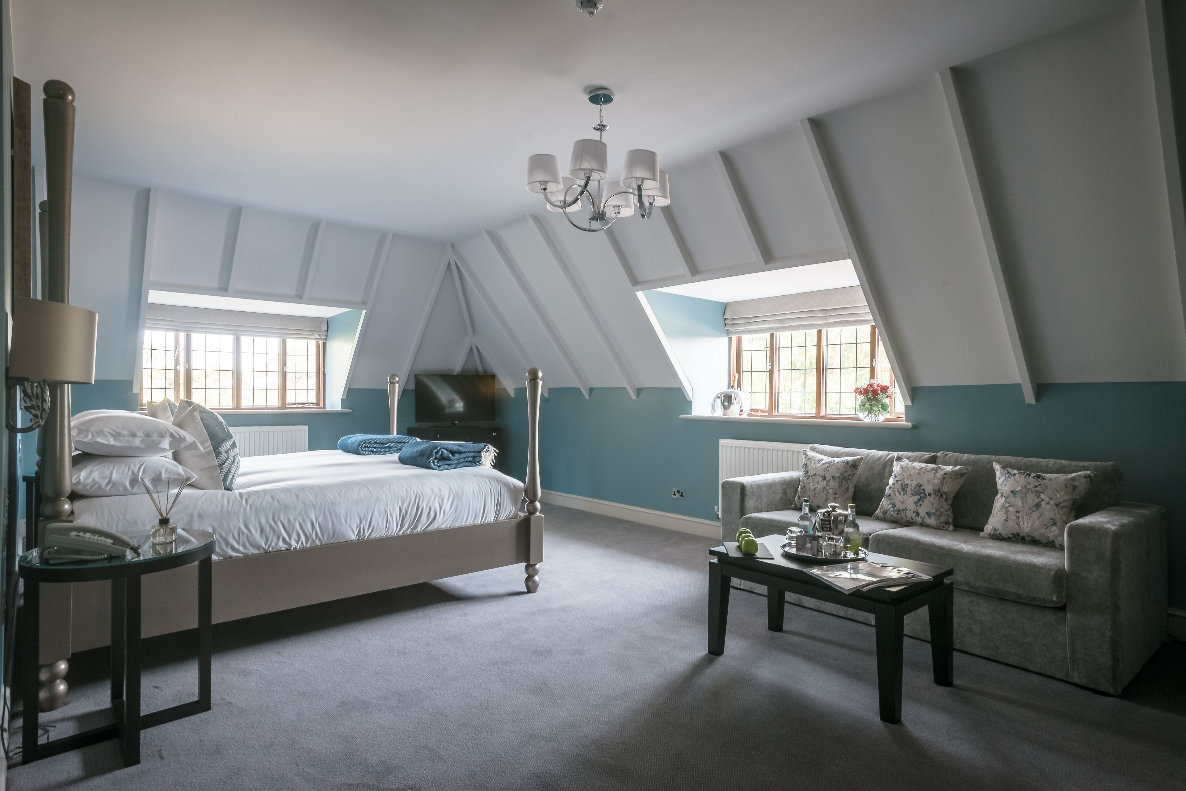 A bedroom with a bed, a nightstand, a coffee table, a sofa, and a chandelier.