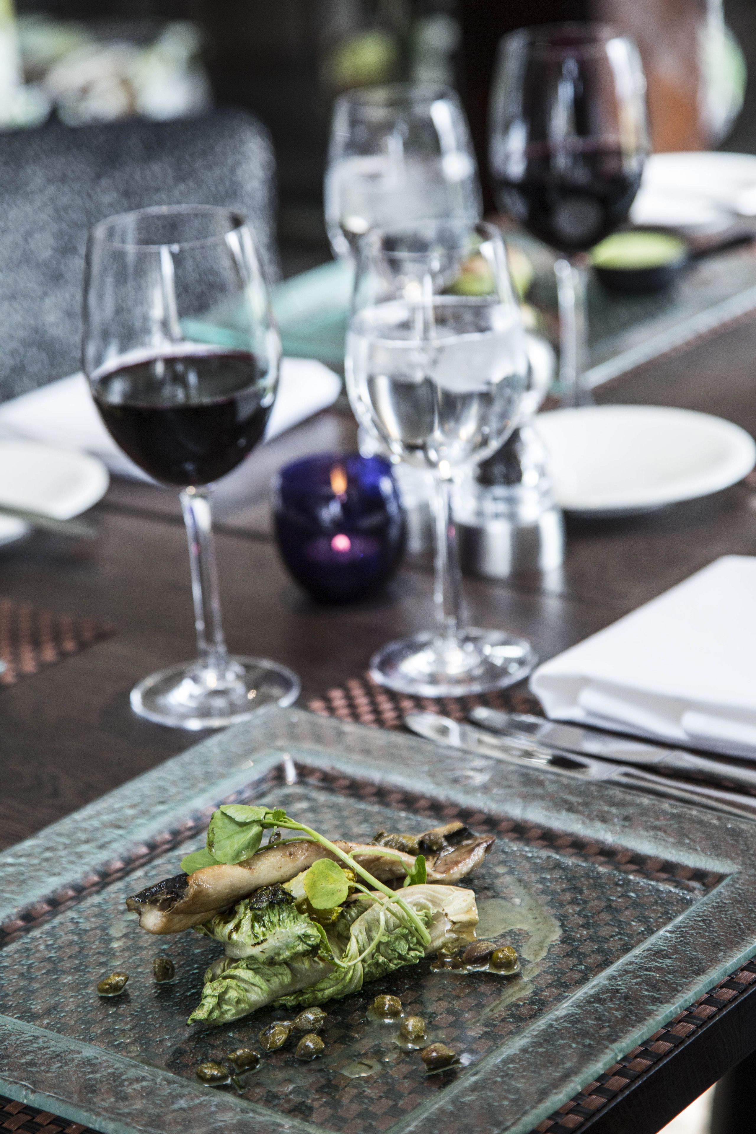A dining table with a glass plate of food, wine glasses, and a purple decorative item.