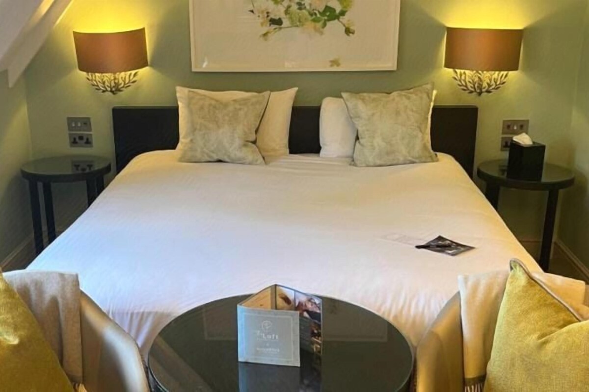 Habitación de hotel con una cama grande, dos mesitas de noche, una mesa redonda y dos sillas.