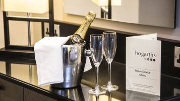 Un minibar con una botella de champán, dos copas y un menú de servicio a la habitación del Hotel Hogarths.
