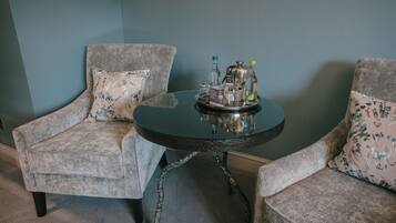 A room with two grey upholstered chairs with floral patterns, a round table with a metal base, and a tray with various bottles and a coffee pot.