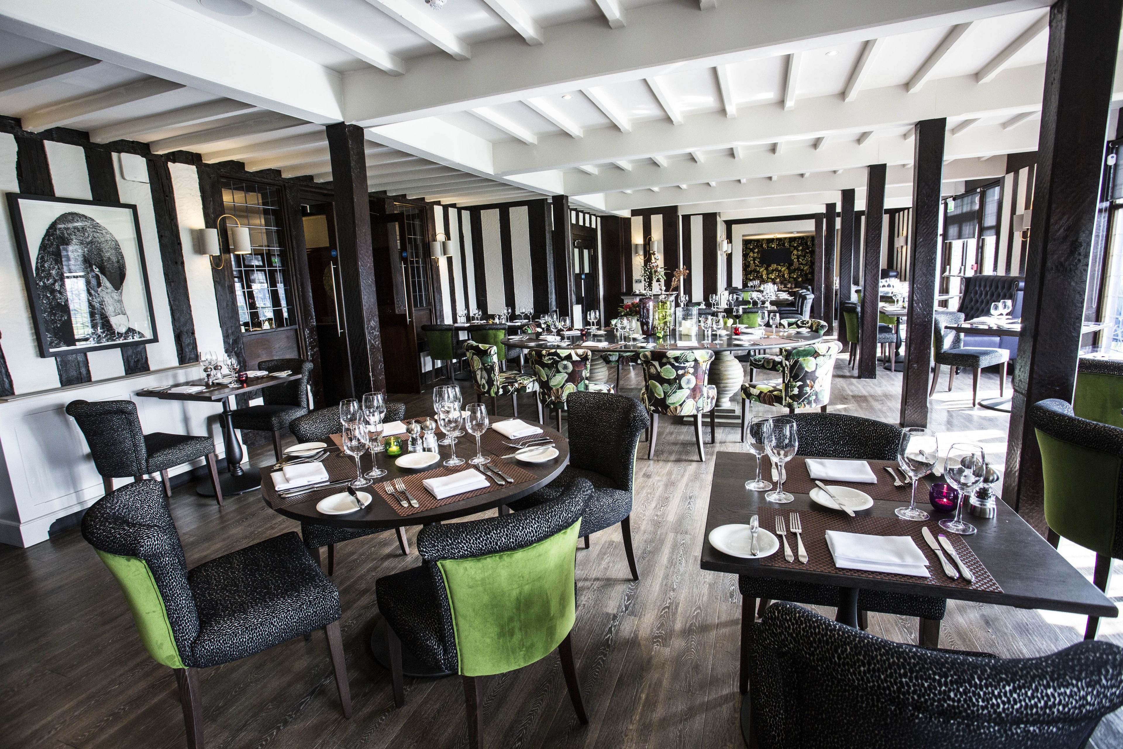 A restaurant with round tables, black and green upholstered chairs, and a modern interior design.