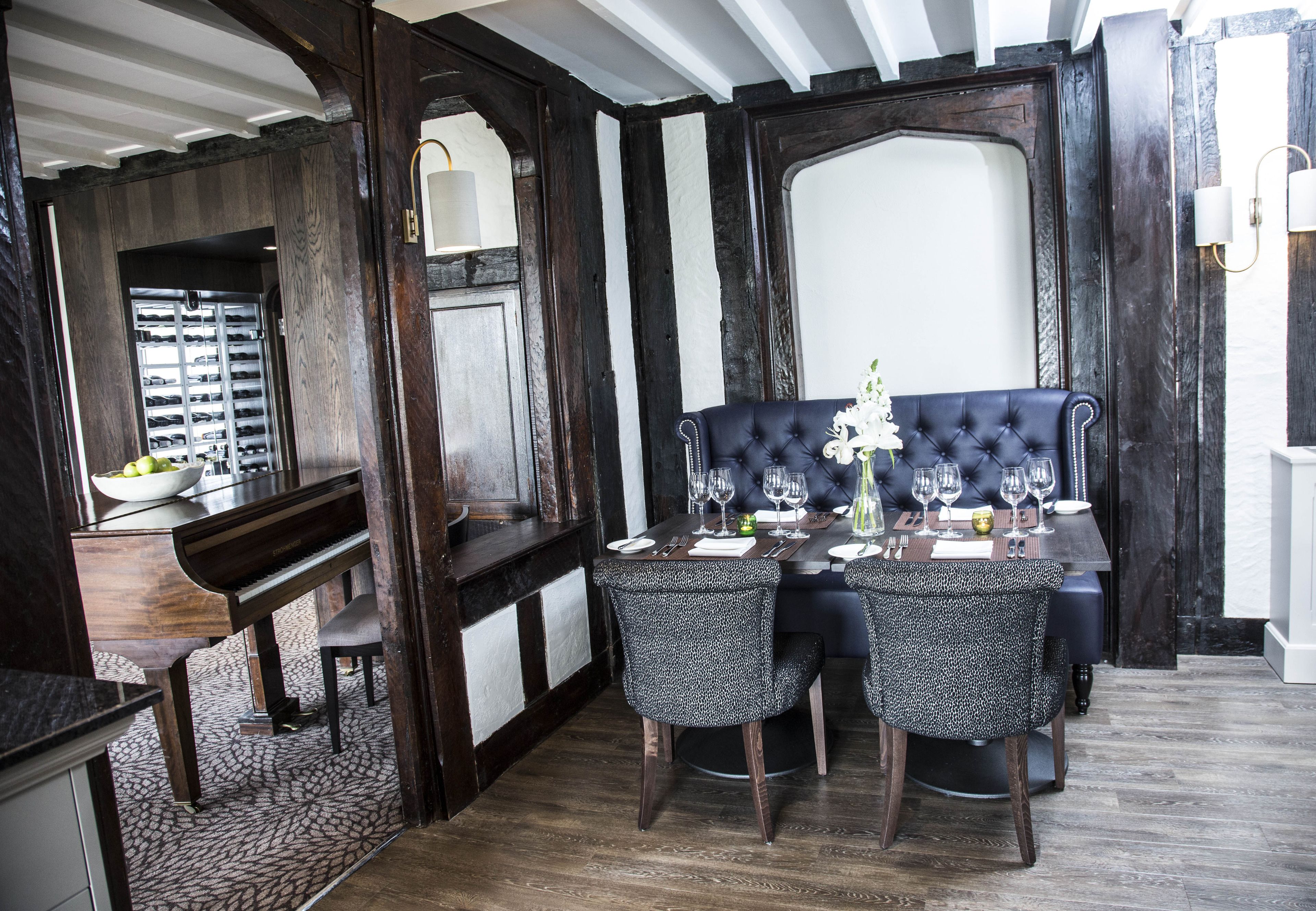 A dining area with a piano, a bench, and a table set for four with chairs.
