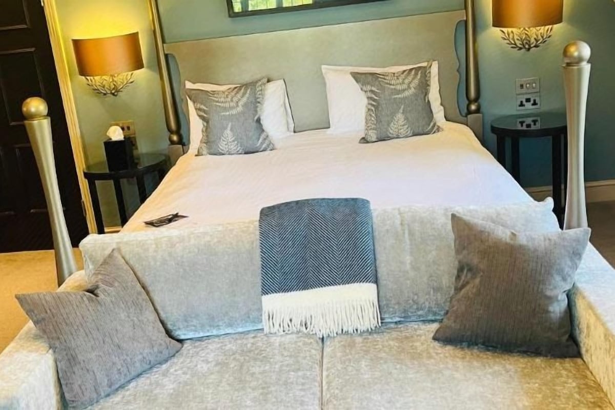 A neatly made bed with pillows and a throw blanket, a bedside table with a lamp, and a wall-mounted light fixture.