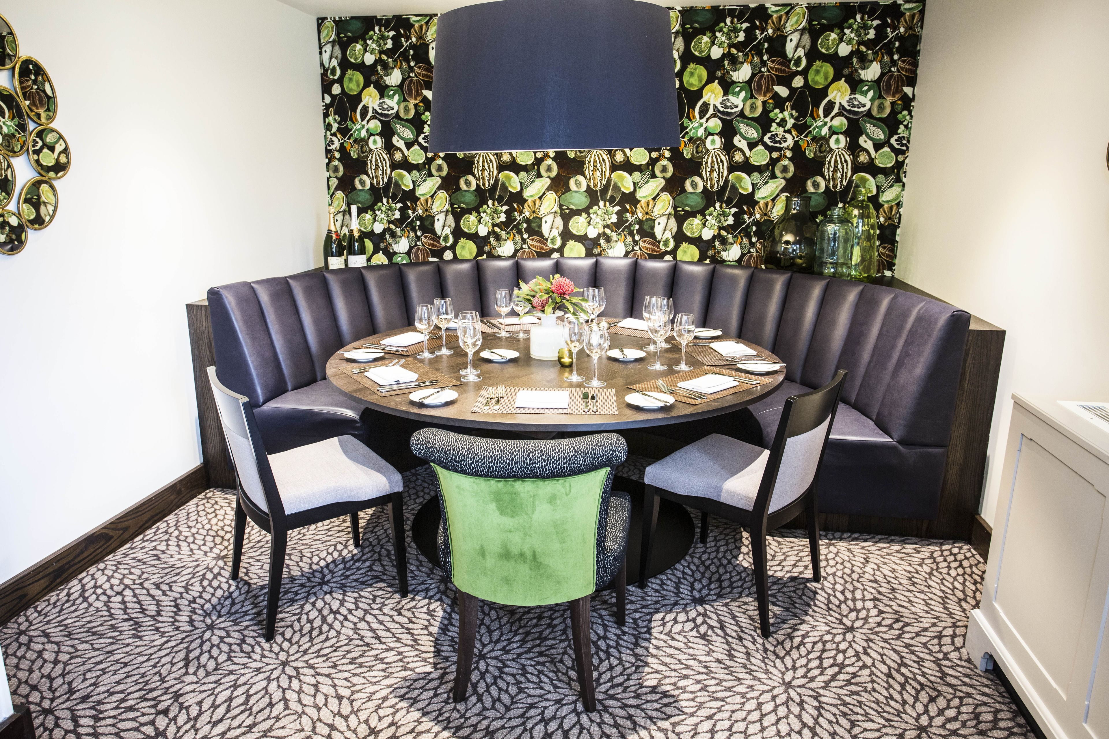 A round table with a dark wood finish, surrounded by upholstered chairs with light grey cushions.