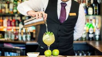 Een bartender schenkt een drankje in een glas, versierd met een partje citroen en munt. Op de bar liggen twee groene appels.