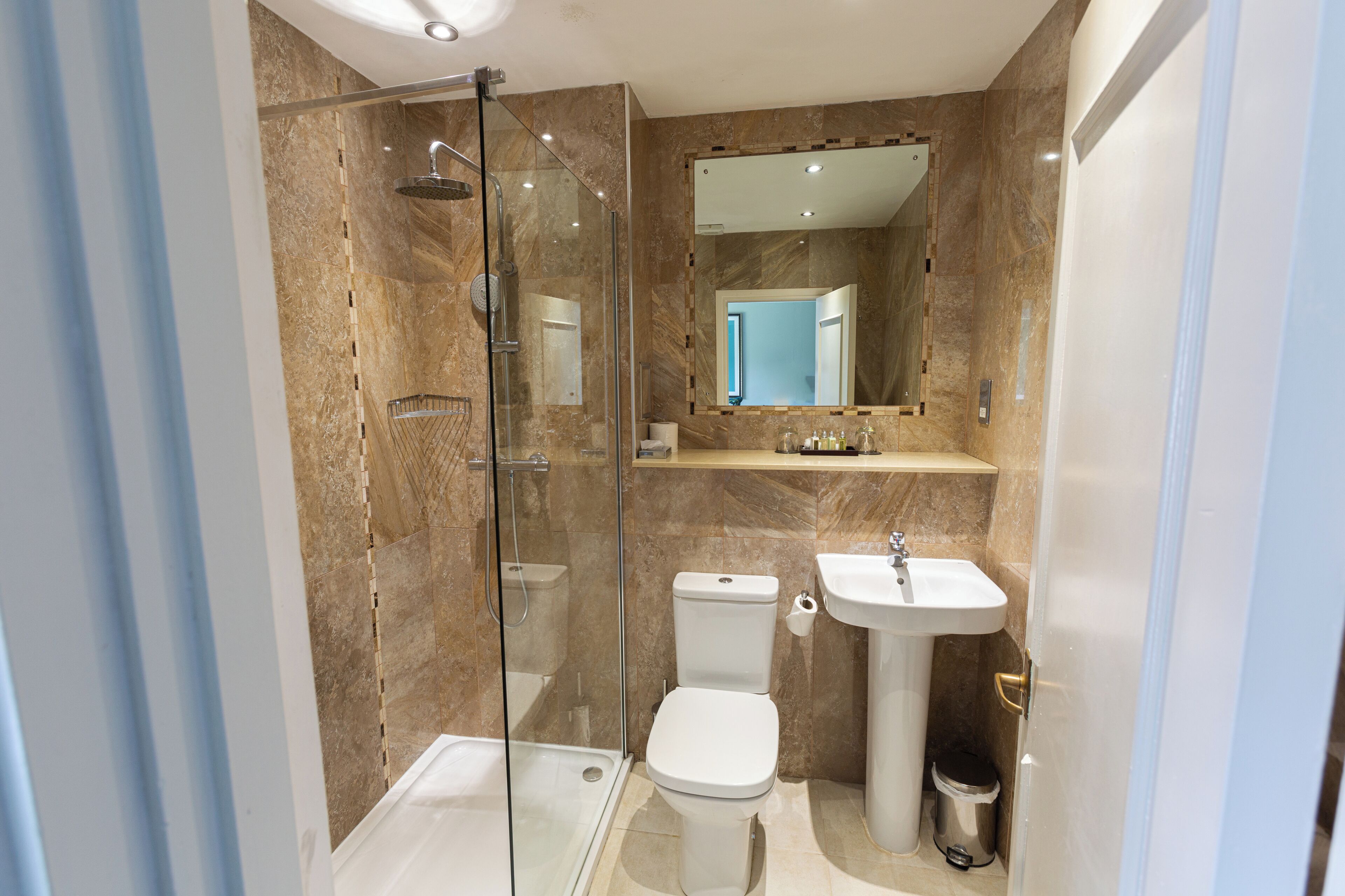 A modern bathroom with a glass-enclosed shower, a toilet, a sink, and a marble-tiled wall.