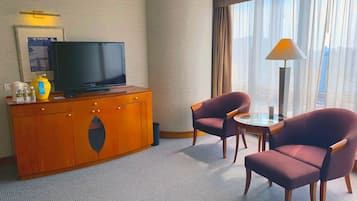 Habitación de hotel con televisor de pantalla plana sobre un mueble de madera, dos sillones, una mesita y una lámpara.
