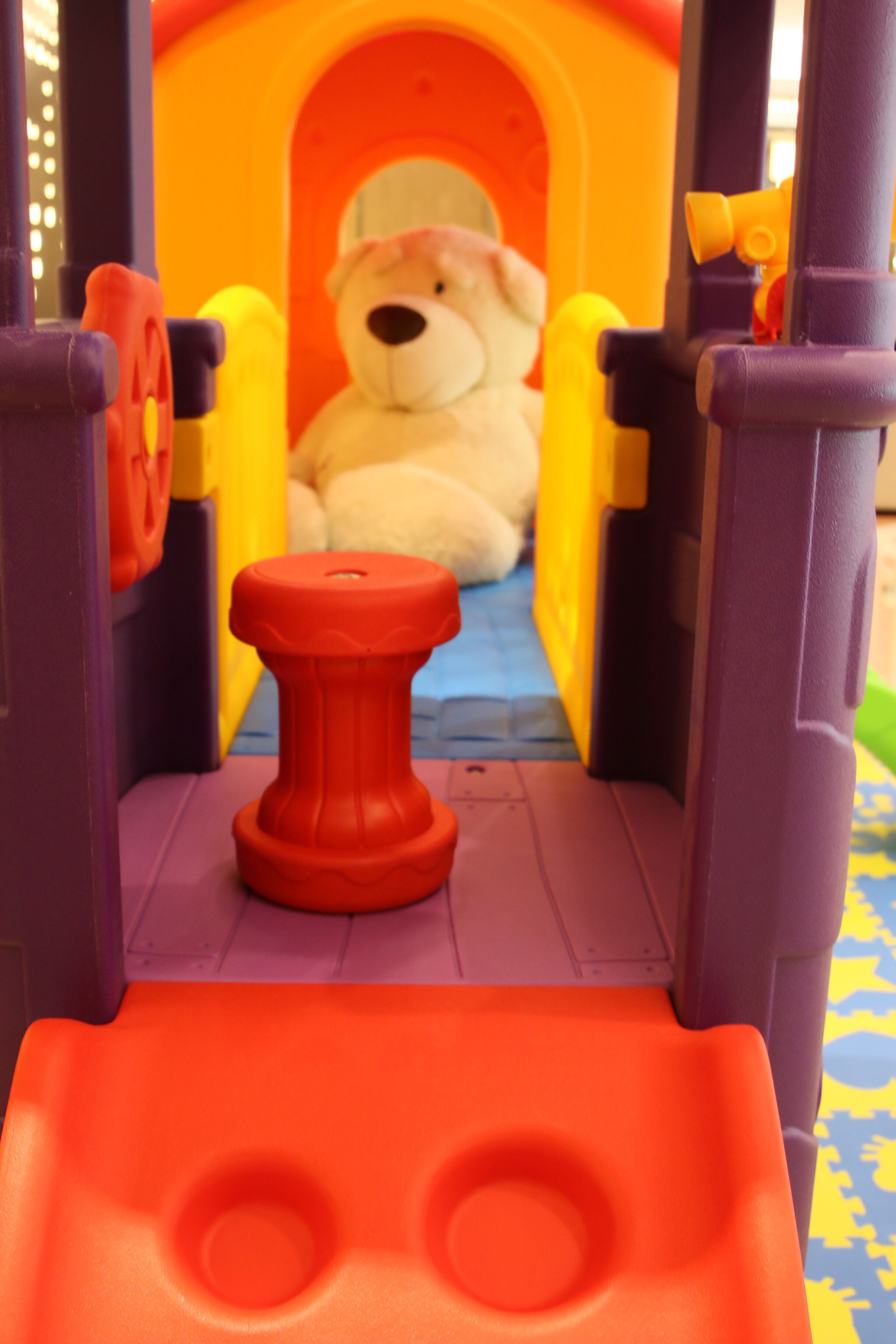 A toy train set with a bear figure inside a tunnel, a red track piece, and a blue and yellow patterned floor.