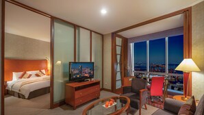 A hotel room with a bed, a television, a desk, a chair, and a view of the cityscape. - Hotel Nikko Dalian (Dalian)