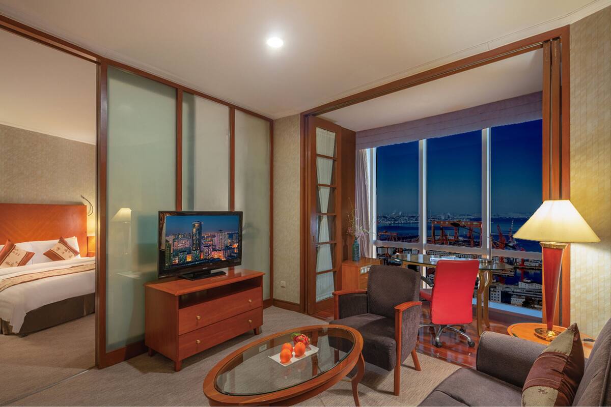A hotel room with a bed, a television, a desk, a chair, and a view of the cityscape.