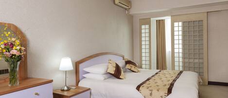 A hotel room with a bed, bedside table, lamp, dresser, and a window with curtains.