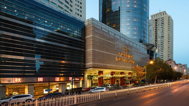 A modern hotel with a prominent glass facade, a curved design, and a visible sign indicating 24-hour service. - Hotel Nikko Dalian (Dalian)