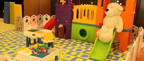 Zona de juegos con un tren, un tobogán y una mesa con bloques de construcción.