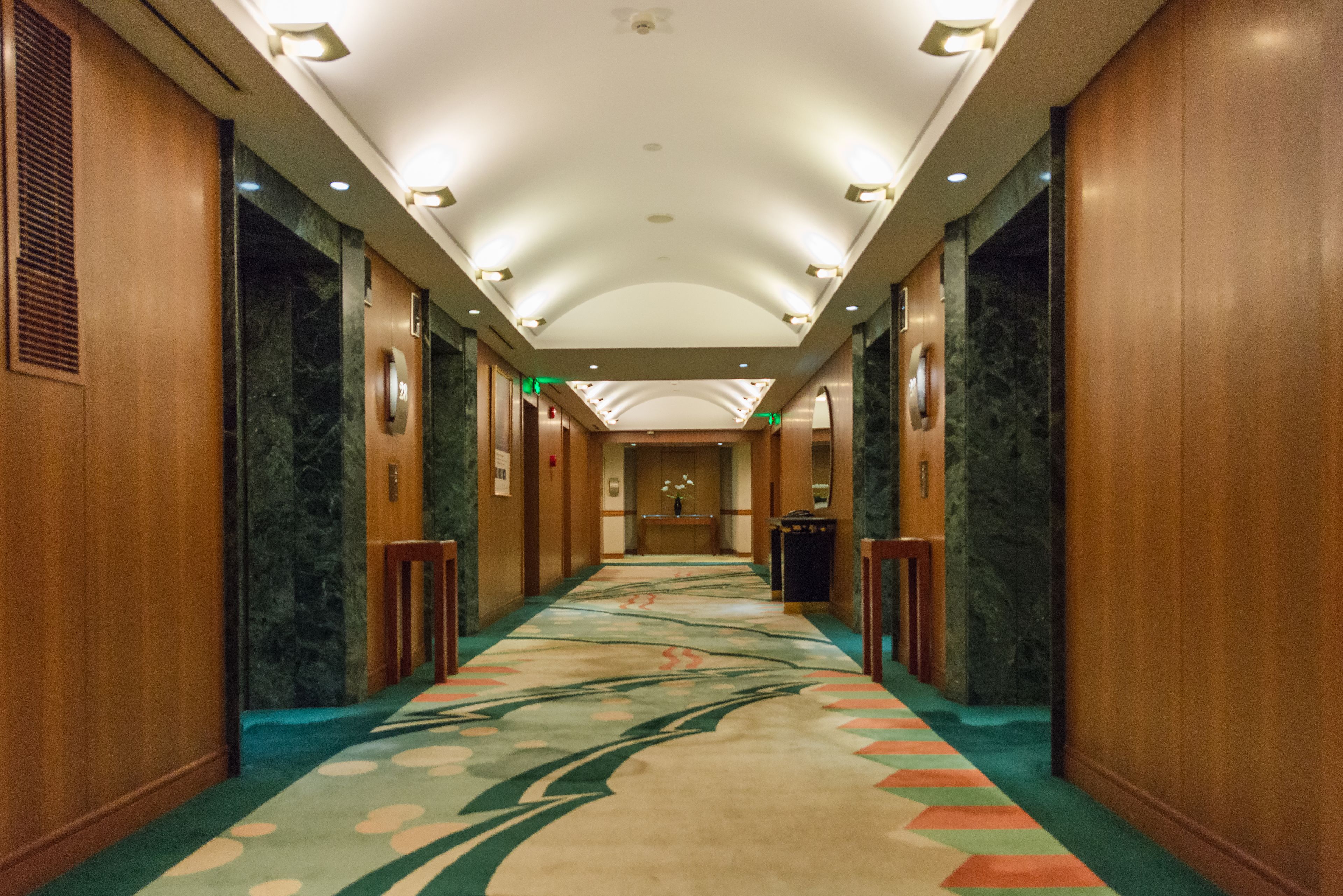 A hotel corridor with a marble floor, wooden walls, and a central light fixture.