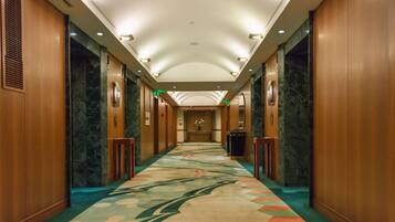A hotel corridor with a marble floor, wooden walls, and a central light fixture.
