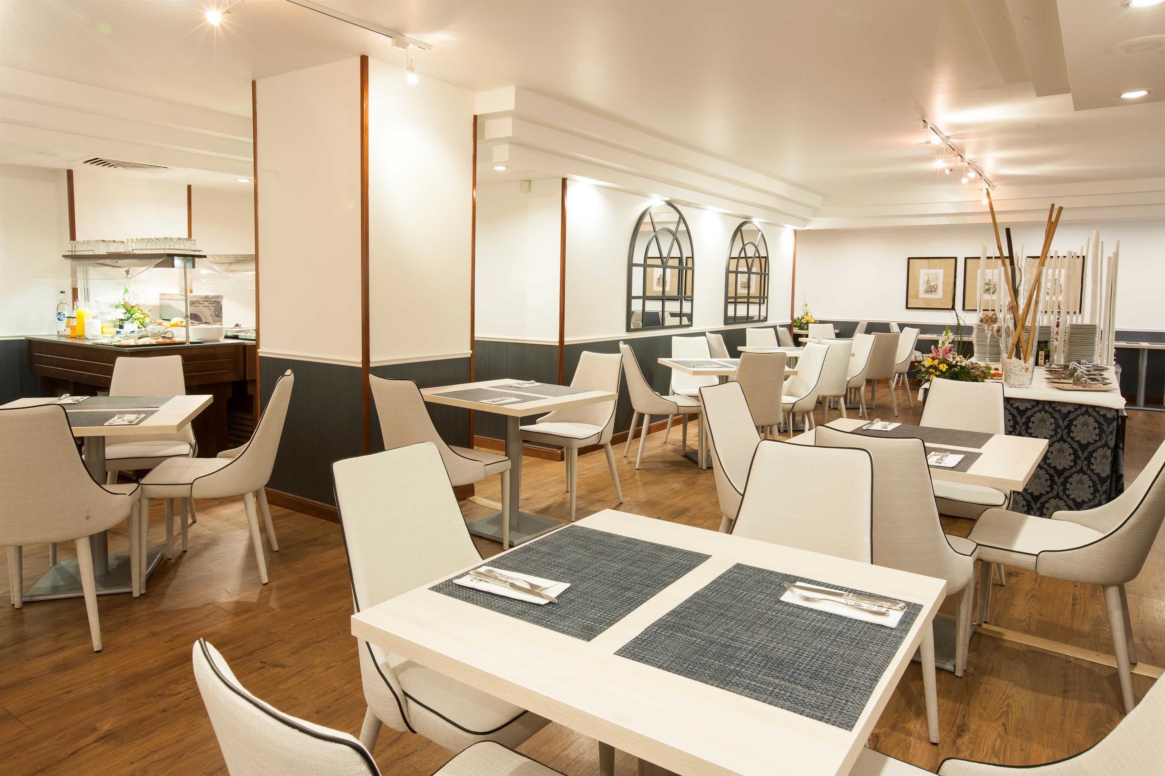 Un restaurante moderno con suelo de madera, sillas blancas y grises, y mesas con manteles individuales.