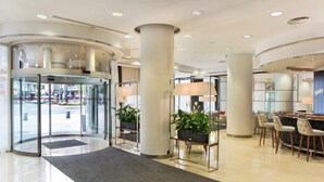 Eine moderne Hotelhalle mit einer Doppeltür, einer Rezeption und einer Sitzecke mit Stühlen und Tischen.