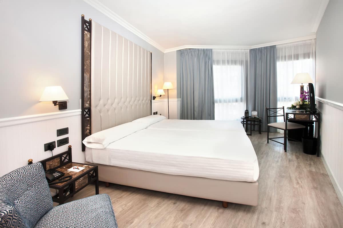 A hotel room with a large bed, bedside tables, a desk, and a chair.