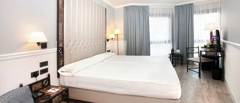 A hotel room with a large bed, bedside tables, a desk, and a chair.