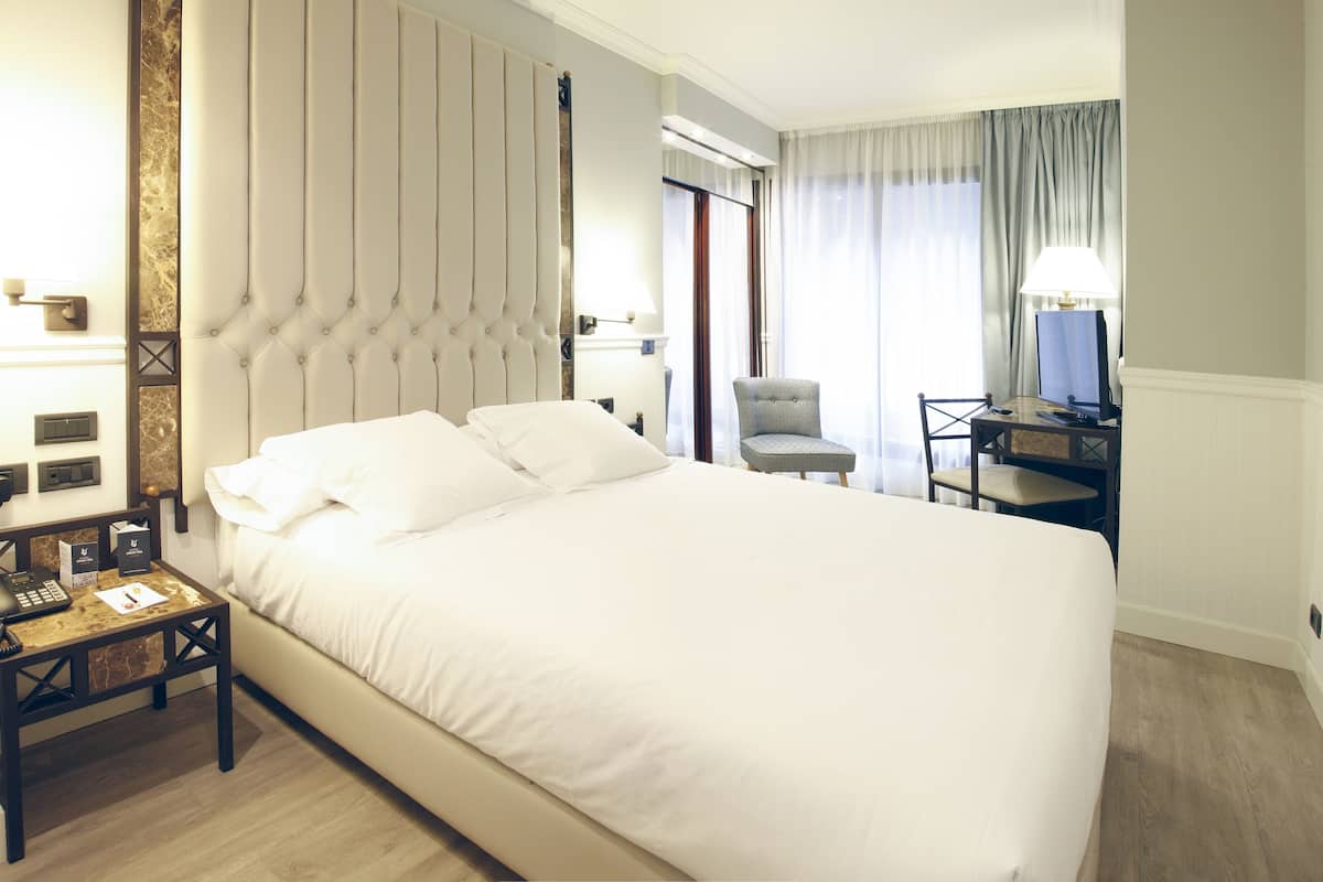 A hotel room with a large bed, a desk with a chair, a television, and a lamp.