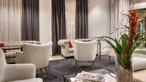 Ein modernes Wohnzimmer mit einer Couch, Sesseln, einem Couchtisch mit Zeitungen und einer Topfpflanze.