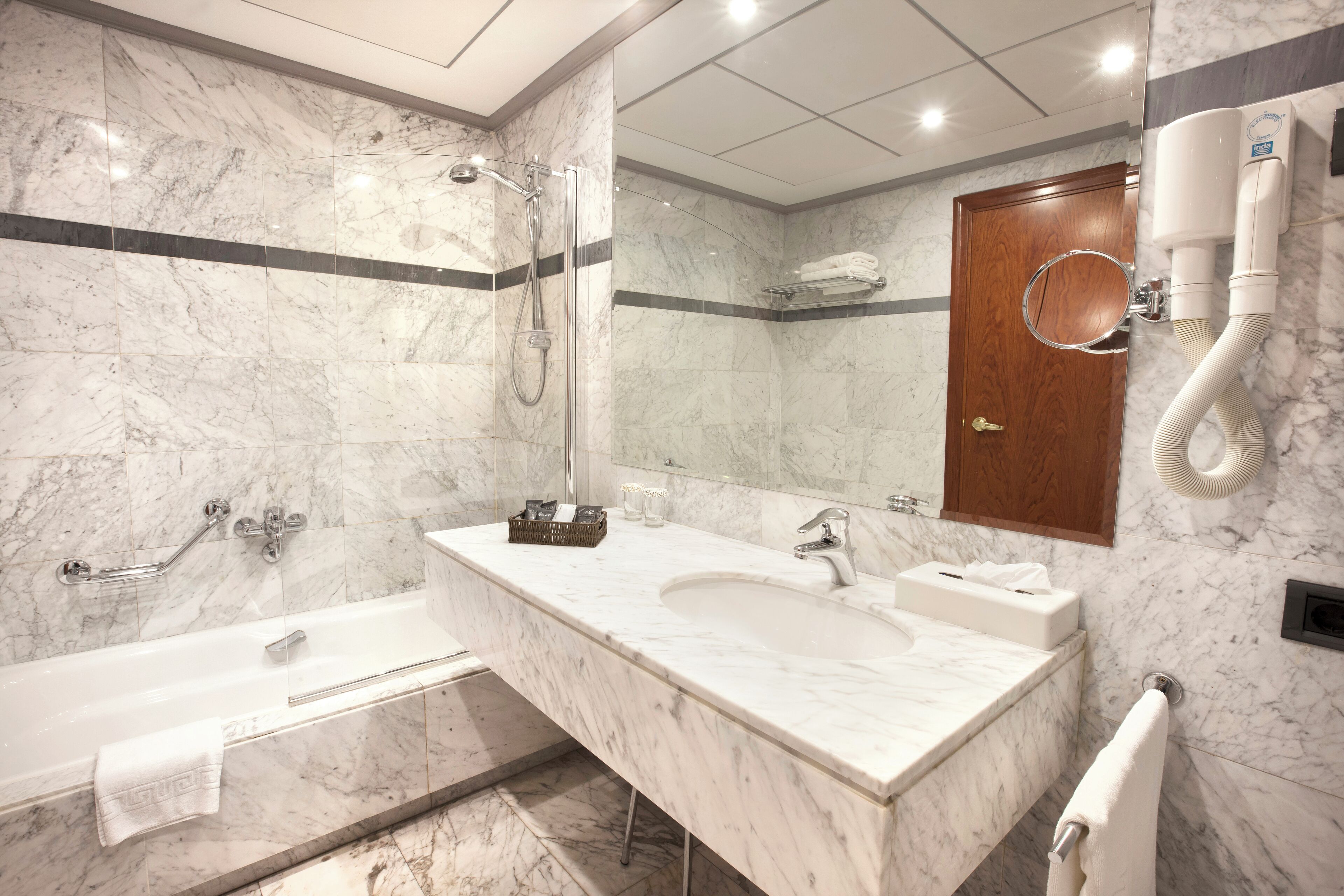Un baño moderno con lavamanos de mármol, bañera, ducha y un espejo grande.