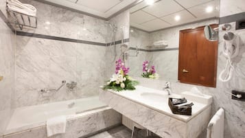 Un baño moderno con suelo de mármol, bañera, un mueble de tocador amplio con espejo y un secador de pelo montado en la pared.