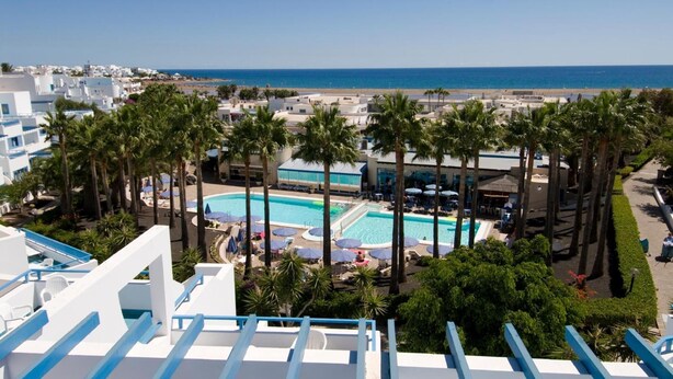 Un resort con zona de piscina rodeada de palmeras, una playa y vistas al mar.
