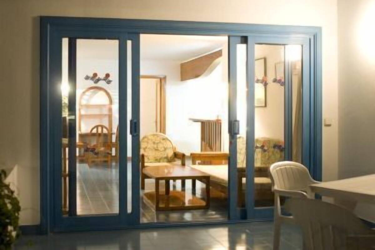 Una habitación con un ventanal corredizo que da a un comedor con una mesa y sillas.