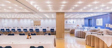 A conference room with multiple tables, chairs, and a buffet setup.