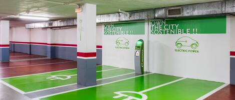 A parking garage with green spaces marked for electric vehicles and signs promoting city sustainability.