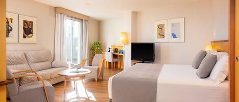 A hotel room with a bed, a sofa, a chair, a desk with a lamp, and a TV.