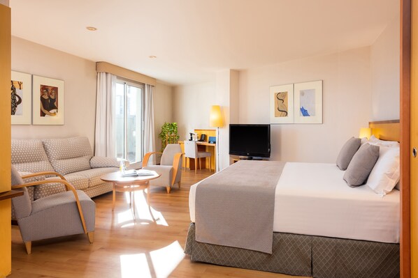 A hotel room with a bed, a sofa, a chair, a desk with a lamp, and a TV.