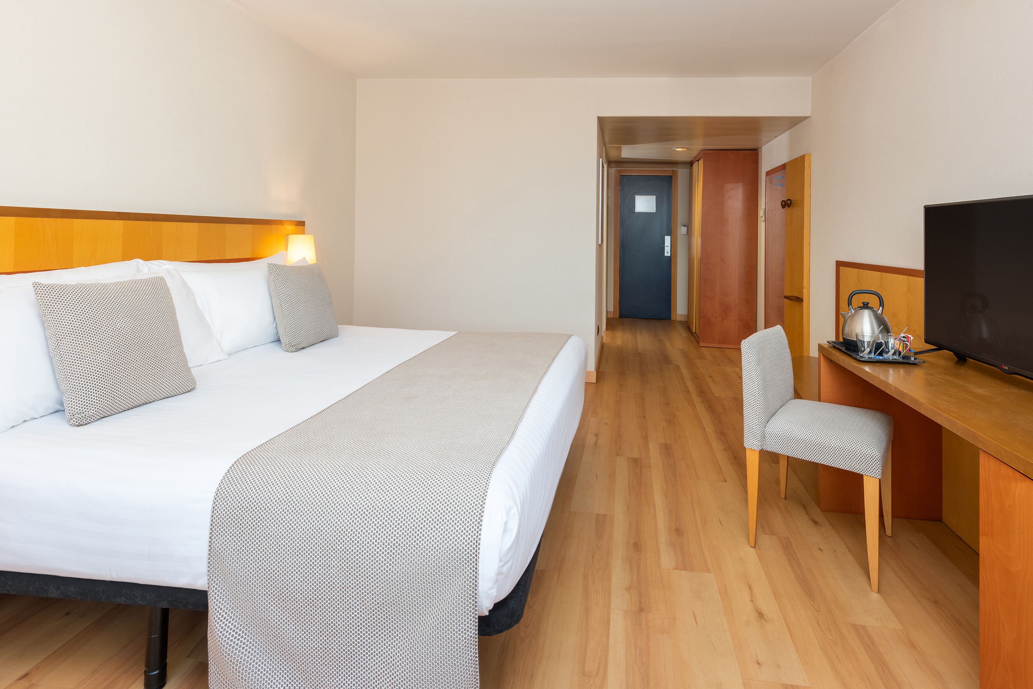 Habitación de hotel con cama, escritorio, silla, televisor y puerta que da a otra habitación.