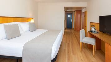Habitación de hotel con cama, escritorio, silla, televisor y puerta que da a otra habitación.