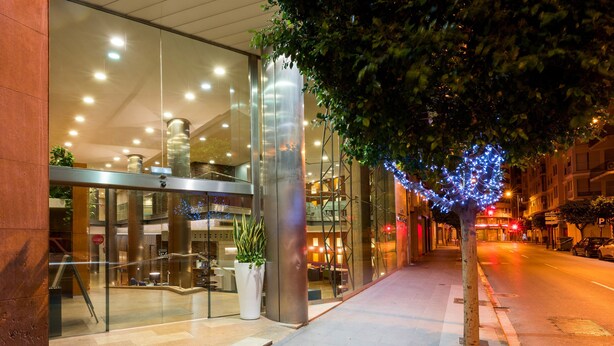 A modern building with a glass facade, a staircase, and a tree with blue lights. - Hotel Castellon Center Affiliated by Meliá (Castelló de la Plana)