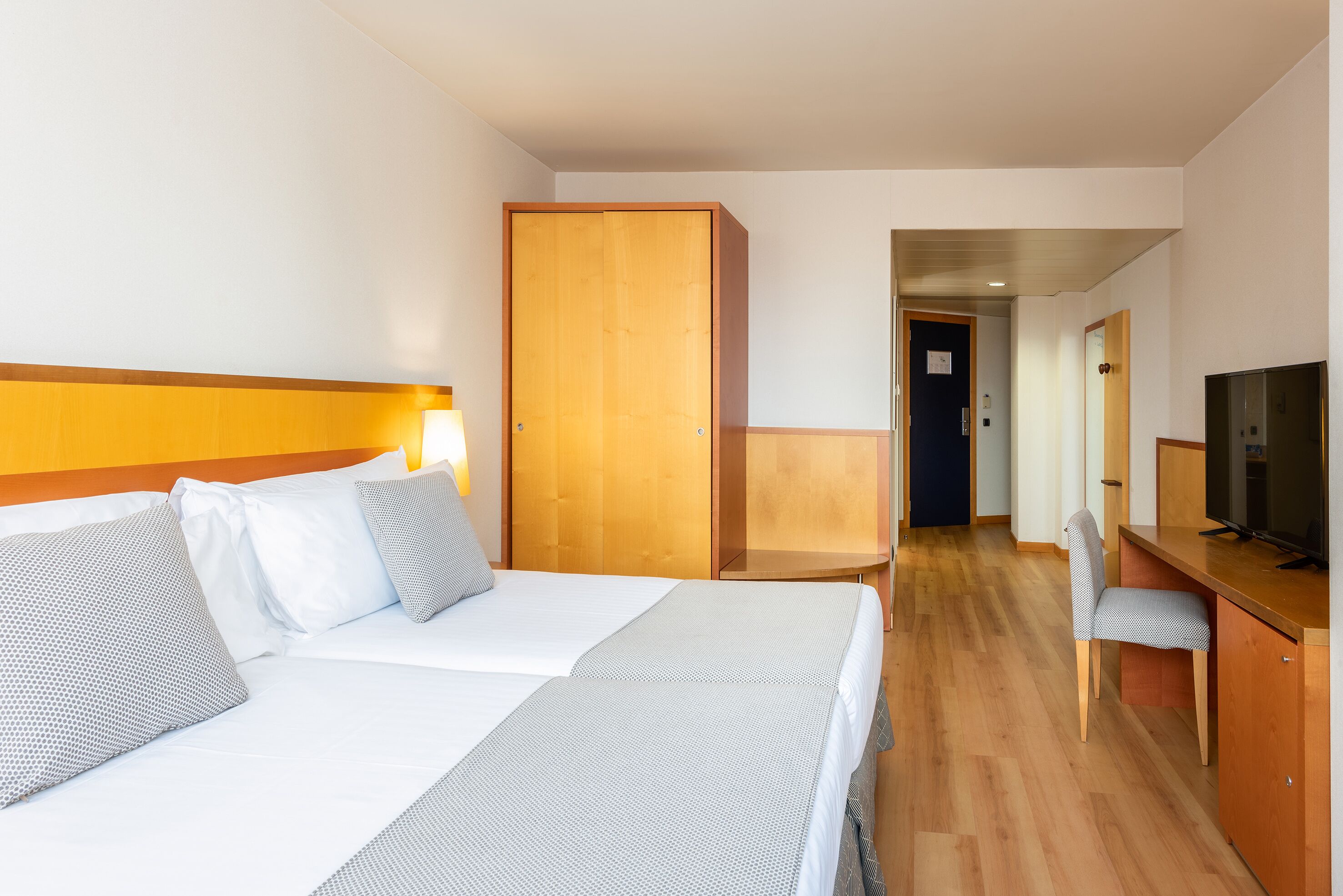 Una habitación de hotel con dos camas, un armario de madera, un escritorio con silla y un televisor.