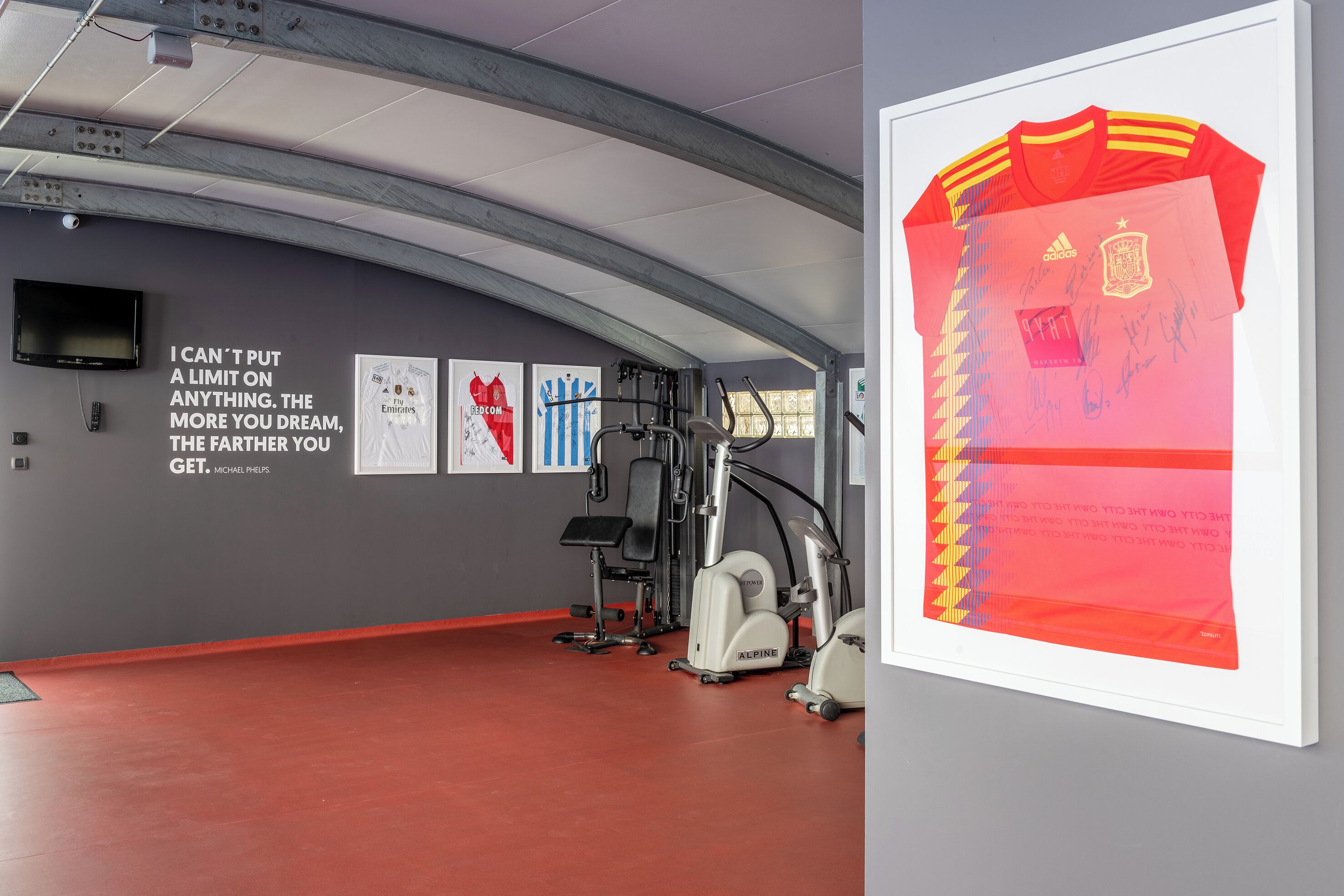 A gym with exercise equipment, motivational posters, and a large framed jersey with signatures.
