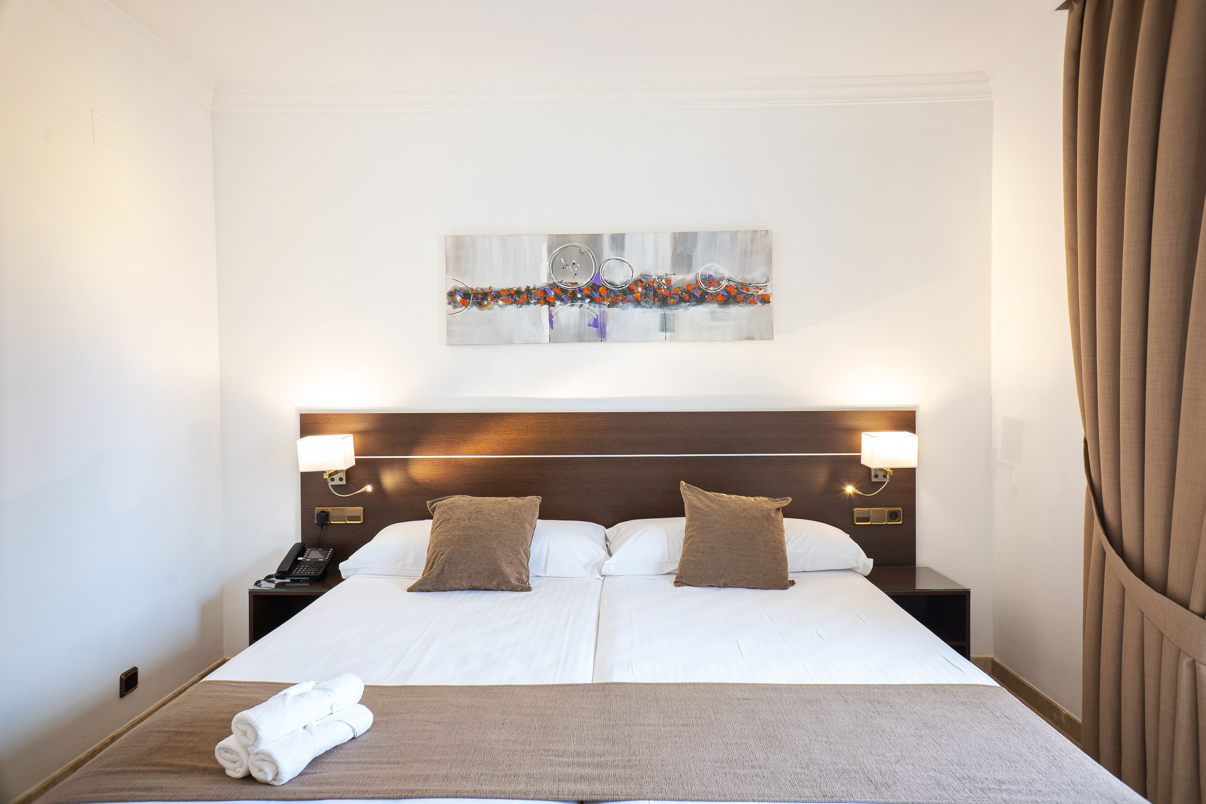A hotel room with a large bed, two bedside tables, a telephone, and a wall-mounted artwork.